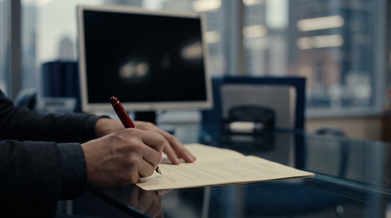 Manos firmando un documento sobre un escritorio de vidrio
